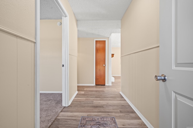 hall with light wood-style floors, a wainscoted wall, and a textured ceiling