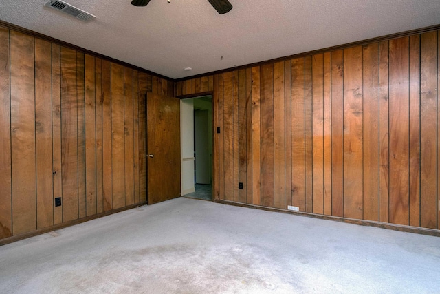 unfurnished room with wood walls, visible vents, a textured ceiling, and light colored carpet