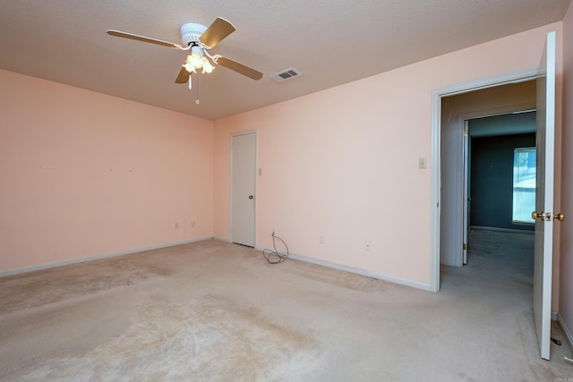 spare room with light colored carpet, visible vents, a ceiling fan, a textured ceiling, and baseboards