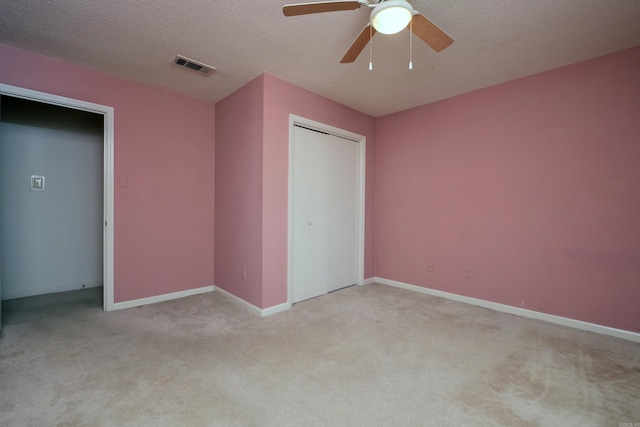 unfurnished bedroom featuring a textured ceiling, light carpet, visible vents, baseboards, and a closet