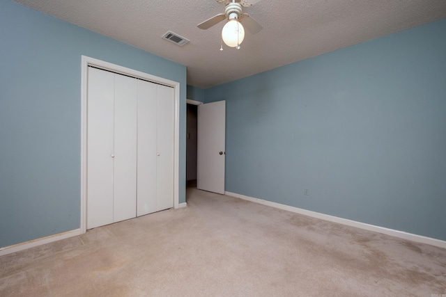 unfurnished bedroom featuring a textured ceiling, light colored carpet, visible vents, baseboards, and a closet