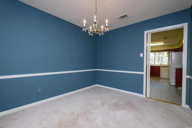 unfurnished room featuring a textured ceiling, carpet flooring, visible vents, baseboards, and an inviting chandelier