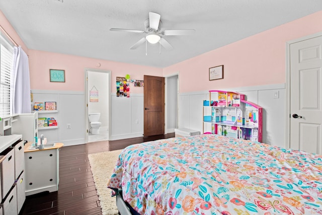 bedroom with connected bathroom, wainscoting, ceiling fan, dark wood-style flooring, and a textured ceiling