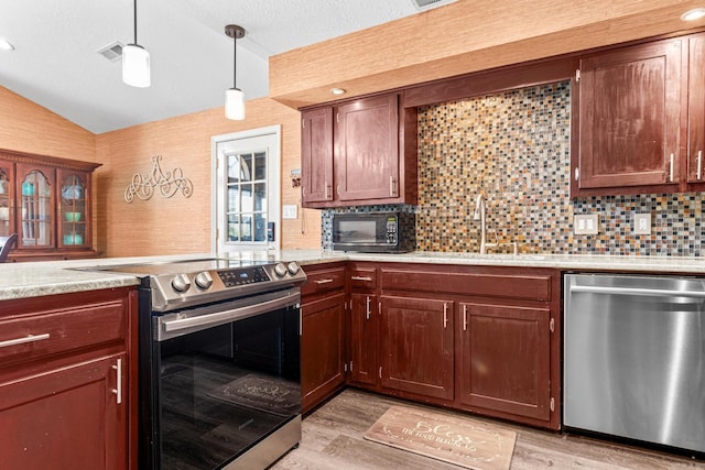 kitchen featuring pendant lighting, light countertops, appliances with stainless steel finishes, vaulted ceiling, and light wood-type flooring