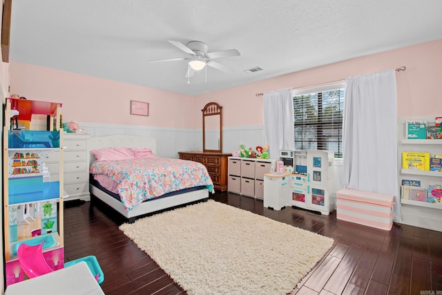 bedroom featuring a textured ceiling, ceiling fan, visible vents, wainscoting, and dark wood finished floors