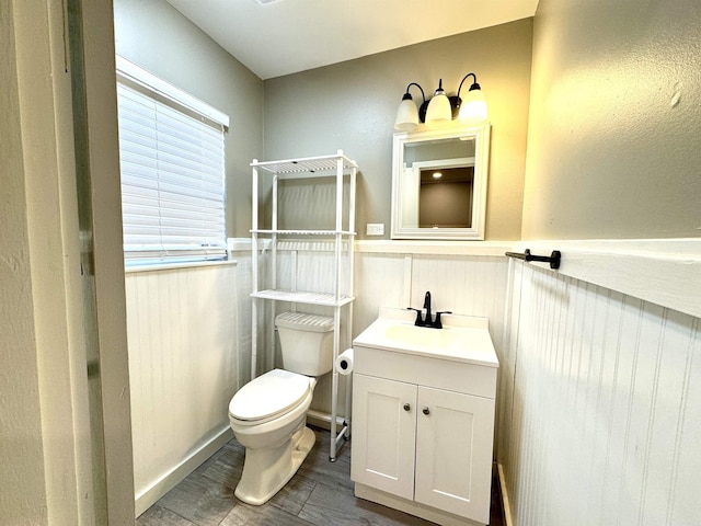 half bath with wood finished floors, wainscoting, vanity, and toilet