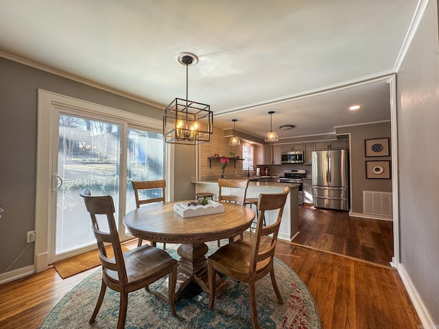 dining space featuring dark wood finished floors, visible vents, crown molding, and baseboards