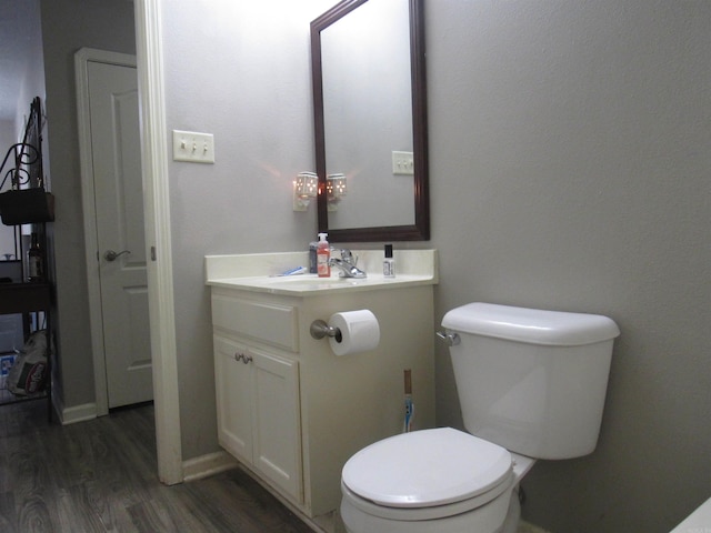 half bathroom featuring toilet, wood finished floors, vanity, baseboards, and a closet