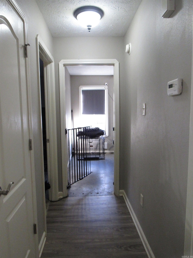 hall with a textured ceiling, dark wood finished floors, and baseboards