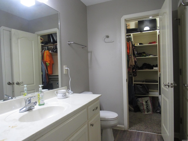 bathroom with a walk in closet, vanity, toilet, and wood finished floors