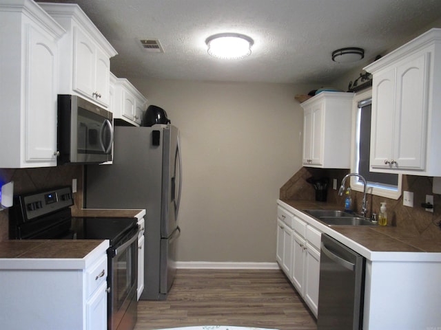 kitchen with stainless steel appliances, tile counters, tasteful backsplash, white cabinets, and a sink