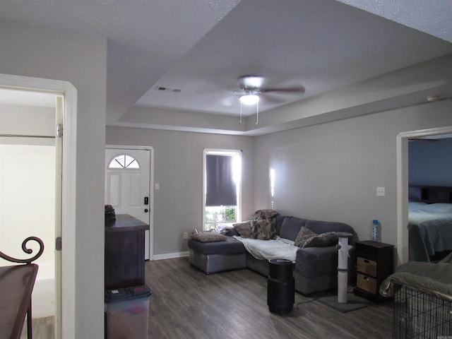 living room featuring dark wood-style floors, a tray ceiling, ceiling fan, and baseboards