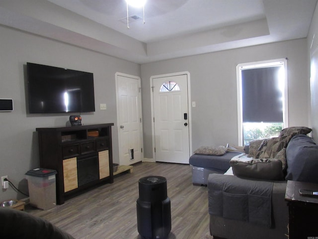 living room featuring a raised ceiling, visible vents, and wood finished floors