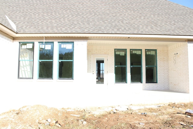 exterior space featuring a patio area, brick siding, and a shingled roof