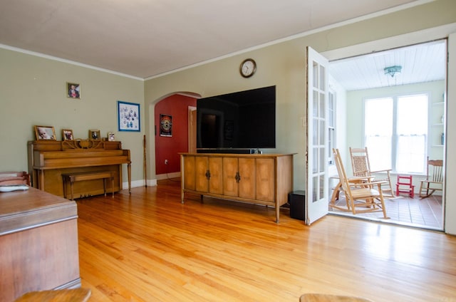 living area featuring light wood-style flooring, arched walkways, baseboards, and ornamental molding