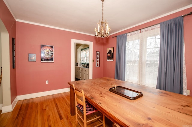 dining space featuring ornamental molding, arched walkways, baseboards, and wood finished floors