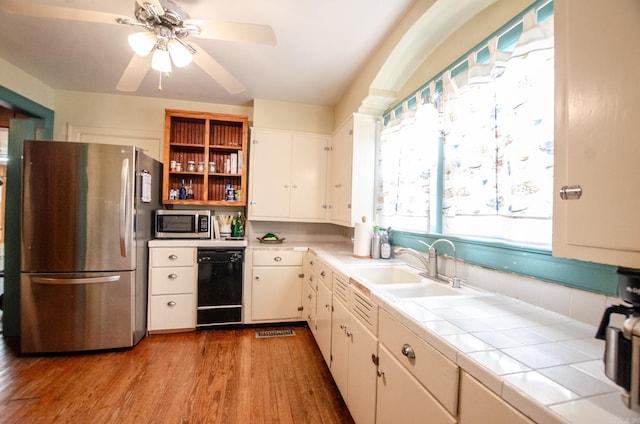 kitchen with tile counters, appliances with stainless steel finishes, white cabinetry, a sink, and light wood-type flooring