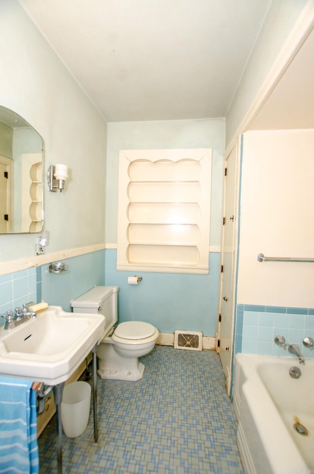 bathroom with baseboards, visible vents, toilet, a bath, and a sink