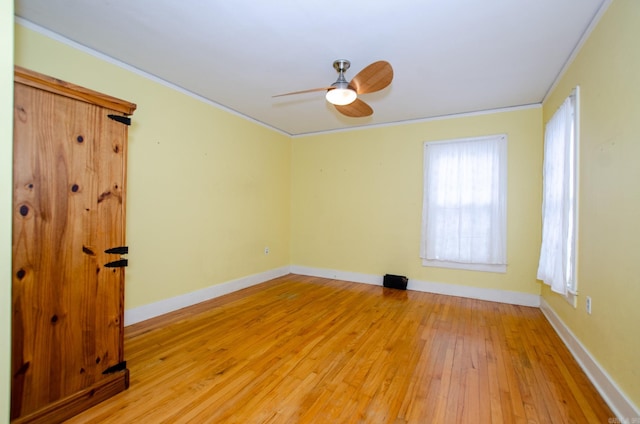 empty room featuring light wood-style floors, a ceiling fan, baseboards, and crown molding