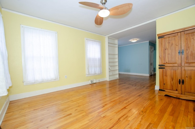 empty room with crown molding, visible vents, light wood-style floors, ceiling fan, and baseboards