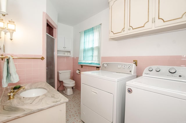 washroom featuring tile walls, washer and clothes dryer, wainscoting, a sink, and laundry area