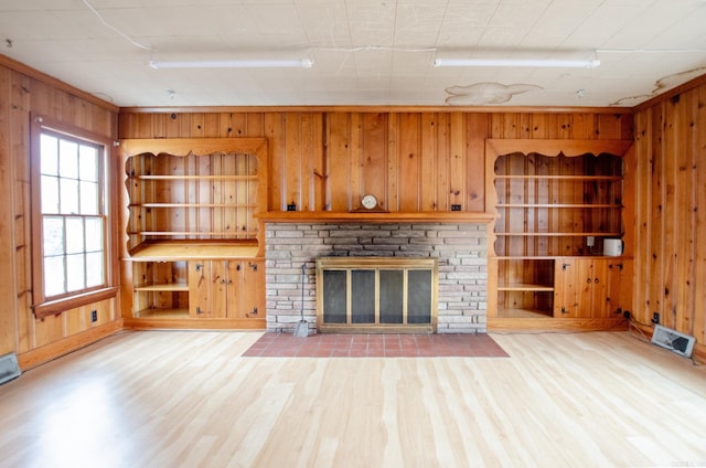 unfurnished living room with wooden walls, visible vents, built in features, and wood finished floors