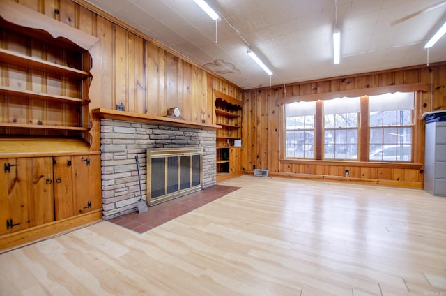 unfurnished living room featuring light wood-style flooring, wooden walls, visible vents, and a fireplace