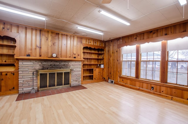 unfurnished living room with a healthy amount of sunlight, wood walls, a stone fireplace, and wood finished floors