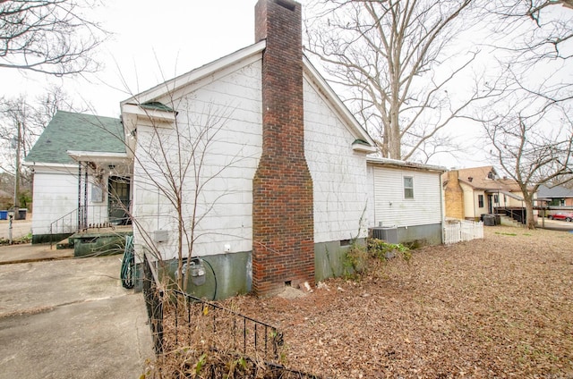 view of home's exterior with a shingled roof, a chimney, and central air condition unit