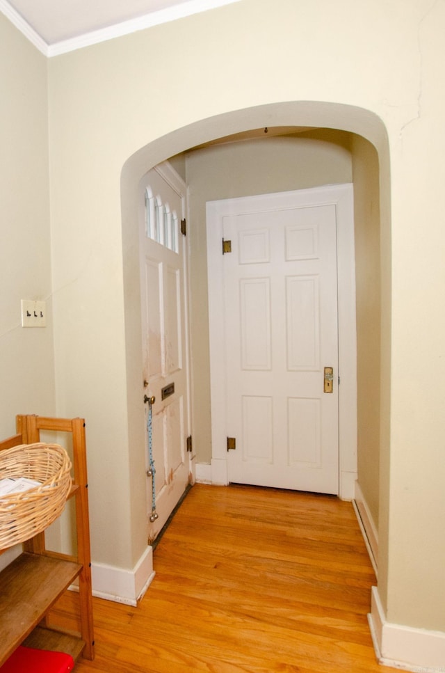 corridor with arched walkways, ornamental molding, wood finished floors, and baseboards