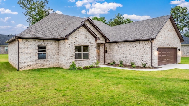 french country style house featuring an attached garage, a shingled roof, a front yard, and brick siding