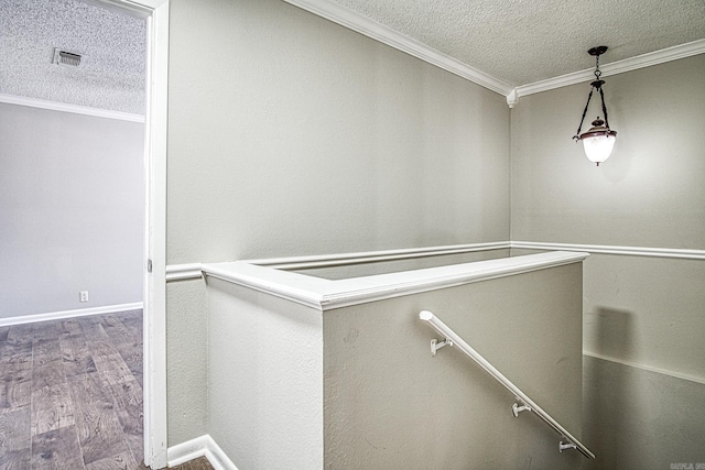 corridor featuring a textured ceiling, wood finished floors, visible vents, an upstairs landing, and crown molding