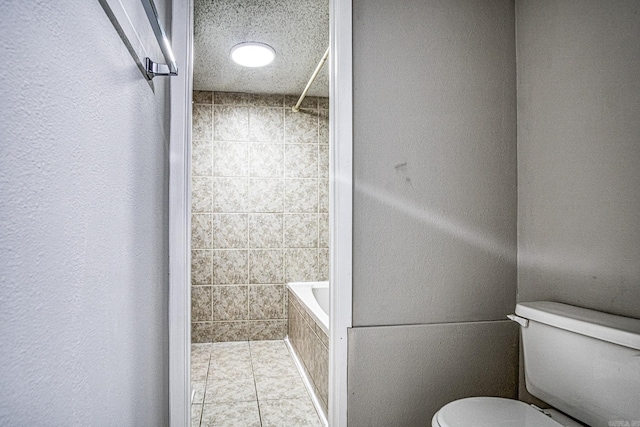 bathroom featuring a textured ceiling, tiled shower / bath, toilet, and tile patterned floors