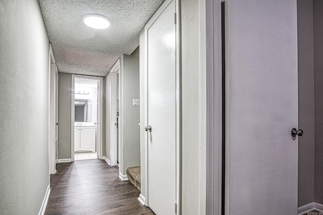 hall featuring baseboards, dark wood-style flooring, a textured ceiling, and a textured wall