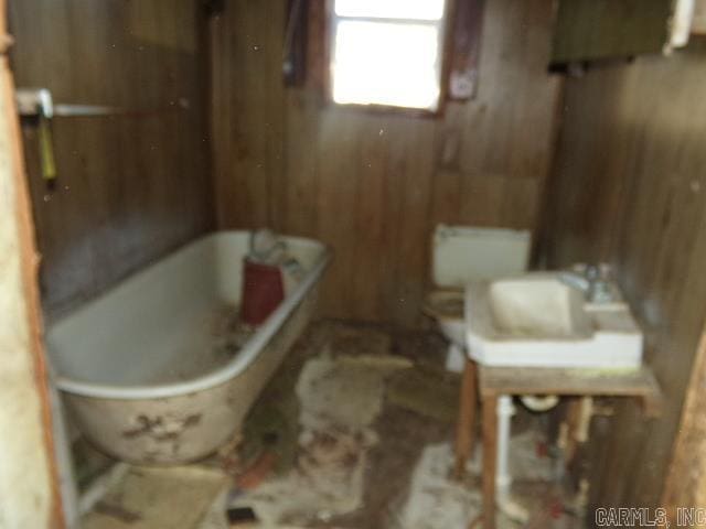 bathroom with a freestanding bath, wooden walls, and toilet