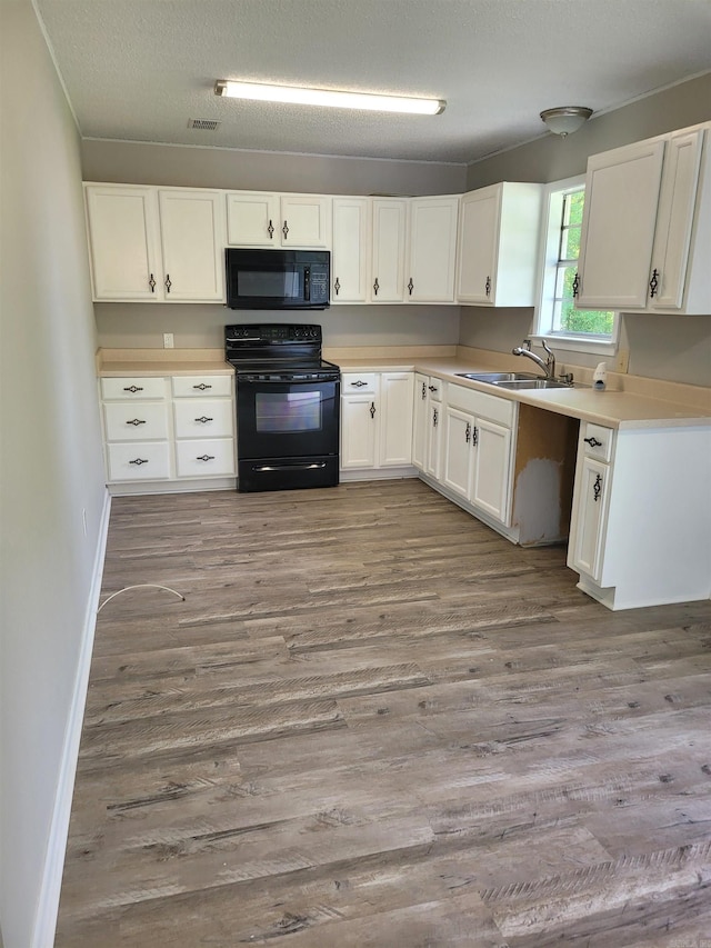 kitchen featuring light countertops, light wood-type flooring, black appliances, white cabinetry, and a sink