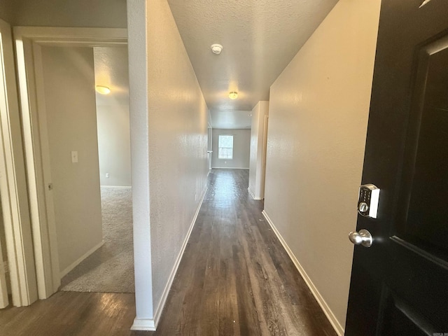 hall featuring baseboards, dark wood finished floors, a textured ceiling, and a textured wall