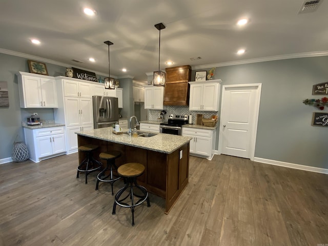 kitchen featuring an island with sink, hanging light fixtures, stainless steel appliances, white cabinetry, and a sink