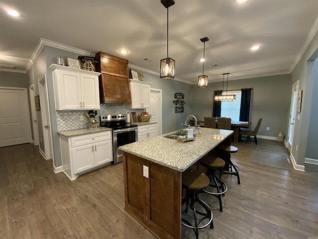 kitchen featuring electric range, an island with sink, white cabinetry, and decorative light fixtures