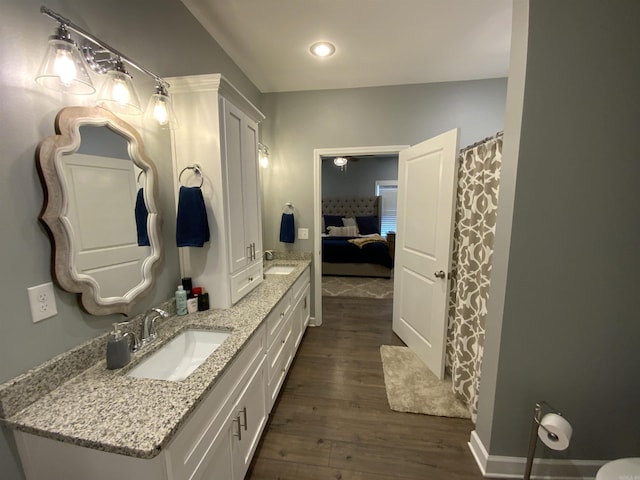 ensuite bathroom featuring connected bathroom, double vanity, a sink, and wood finished floors