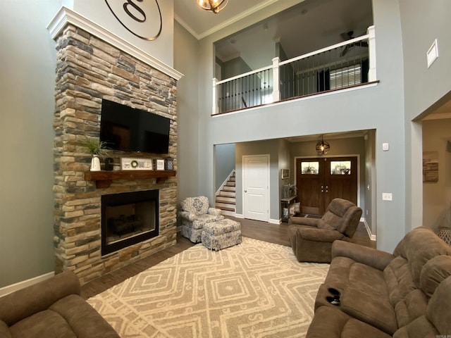 living area featuring ornamental molding, a stone fireplace, baseboards, and wood finished floors