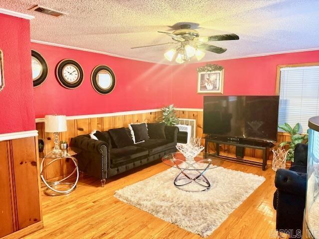 living room featuring a textured ceiling, a wainscoted wall, wood finished floors, visible vents, and ornamental molding