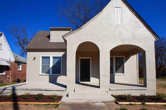 view of front of home with a shingled roof, covered porch, and stucco siding