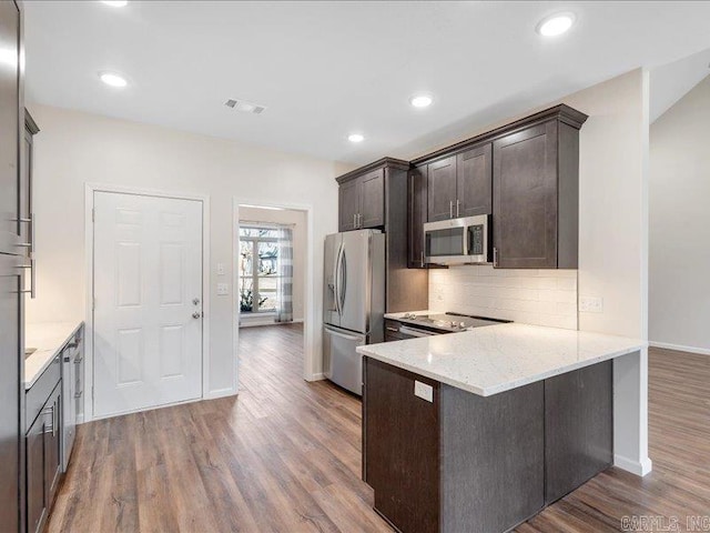 kitchen with light stone counters, wood finished floors, a peninsula, stainless steel appliances, and backsplash