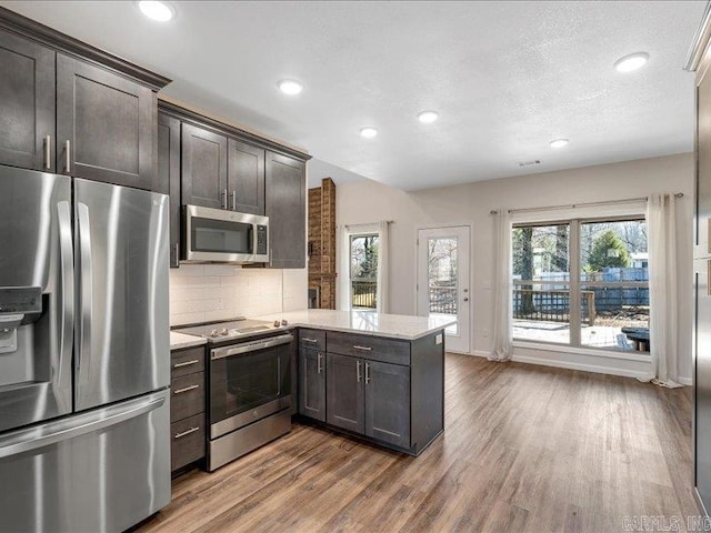 kitchen featuring appliances with stainless steel finishes, backsplash, a peninsula, and dark brown cabinets