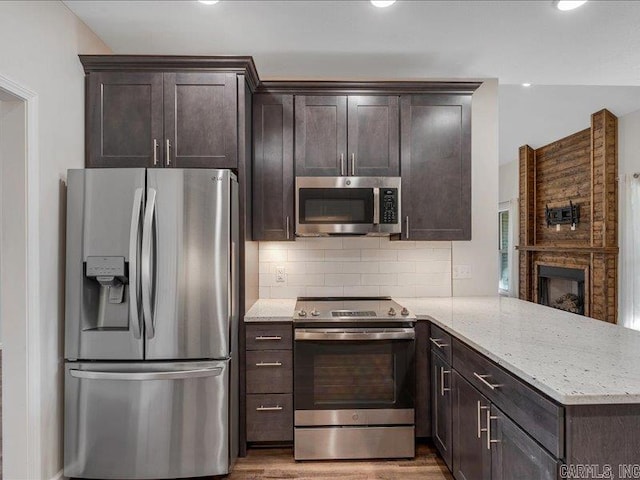 kitchen with backsplash, appliances with stainless steel finishes, dark brown cabinetry, light stone countertops, and a peninsula