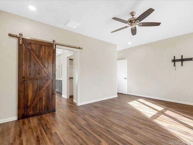 spare room with a barn door, dark wood-type flooring, and baseboards