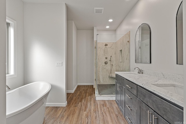 bathroom with visible vents, a sink, wood finished floors, a freestanding tub, and baseboards