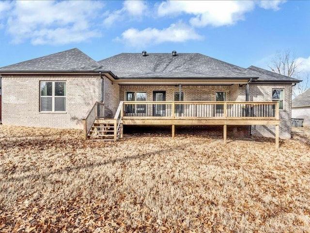 back of property with a deck, brick siding, roof with shingles, and stairs