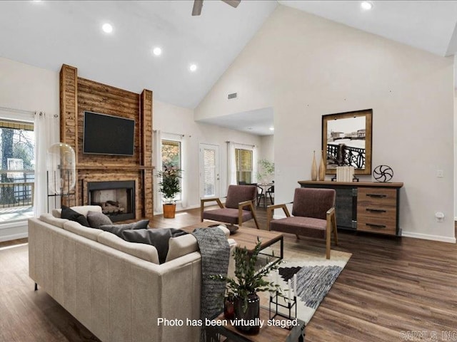 living room featuring dark wood-style flooring, a fireplace, visible vents, high vaulted ceiling, and baseboards